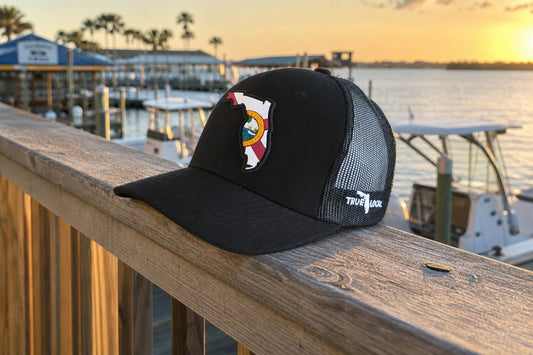 True Local Florida Proud PVC patch trucker hat on a dock railing at a Florida marina at sunset